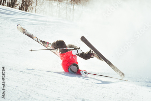 Skier fall down hit head painfully on hard groomed piste with snow swirls on ski resort slope. Sports Injury young skier in professional sports concept.. Reckless