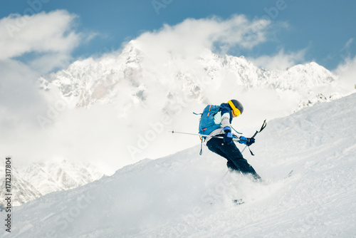 Playful Skier performing switch skiing trick backwards on snowy slope with mountains in background