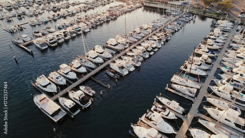 Many boats of various sizes and styles docked peacefully at a serene marina. The waterfront setting creates a calm atmosphere with no people present.