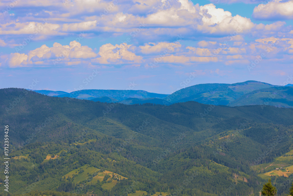 Obraz premium ​A rolling mountain range, covered with emerald-green forests, creates an impressive panoramic view that conveys peace and tranquility.