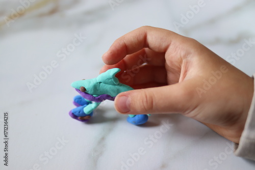 A plasticine figure made by a child in the shape of a shark in children's hands, close-up.