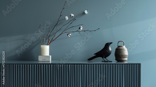 Minimalist still life arrangement with cotton branches and black bird sculpture against blue wall