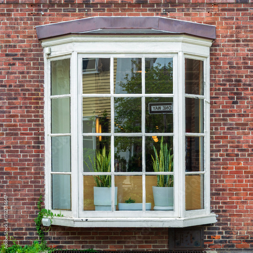 Charming classic bay window framed by a red brick wall with urban reflections inside in Cambridge, Massachusetts, USA
