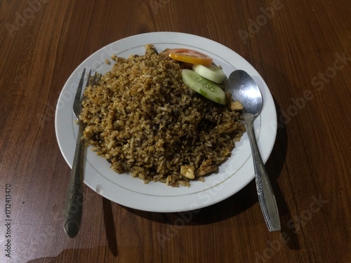 Nasi Goreng: Indonesian fried rice with cucumber and tomato on a white plate.