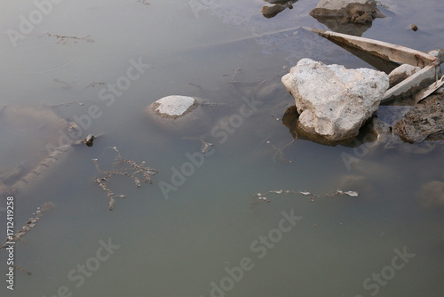 Bild auf Leinwand Surface of stagnant water with floating debris including rocks, wood pieces and sediment