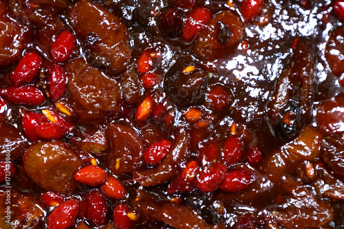 Tableau sur toile Extreme close view of a cooked fruit mixture shows glossy brown date pieces surrounded by ruby red seeds in a thick syrup
