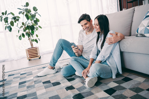 Young couple enjoying leisure time together on the living room floor, bonding over shared moments with a smartphone in hand