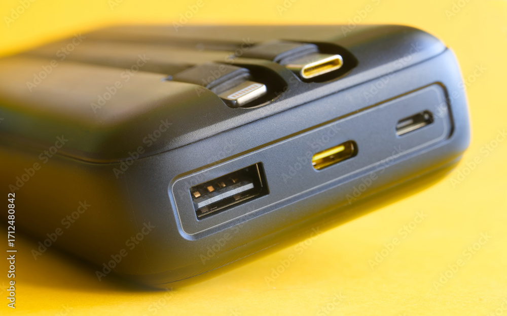 Fototapeta premium High‑capacity power bank on yellow with built‑in USB‑C and Lightning leads plus USB‑C, micro‑USB and USB‑A ports; fast charge hub for phones and tech on the go. Photo
