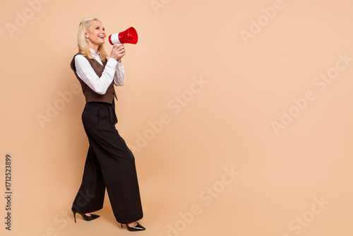 Professional businesswoman in formalwear using a red megaphone against a beige background, expressing enthusiasm and leadership