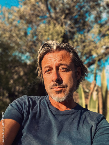 Blond man with beard in blue t-shirt enjoys sun in rural garden.