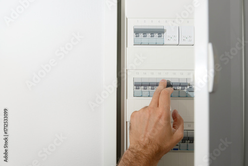 Male hand switching breaker in modern electrical panel box, safe electricity control system.