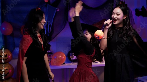 Group of happy asian women in halloween costumes dancing and celebrating together at a spooky party with pumpkins and dark decorations