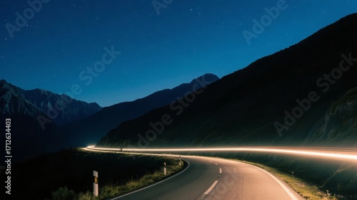 Nighttime mountain road illuminated by car lights under a starry sky
