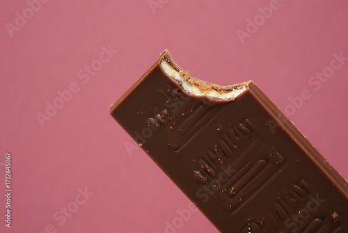 Close up of a bitten chocolate bar against a pink background
