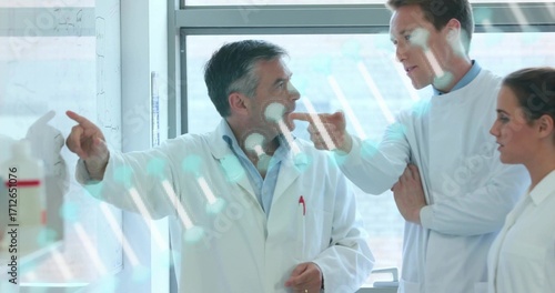 Pointing scientist directing team in lab coats in lab, with whiteboard diagrams and instruments