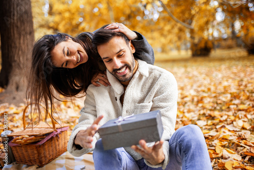 Romantic young couple giving presents to each other in colorful autumn park, joyful and loving fall moment.