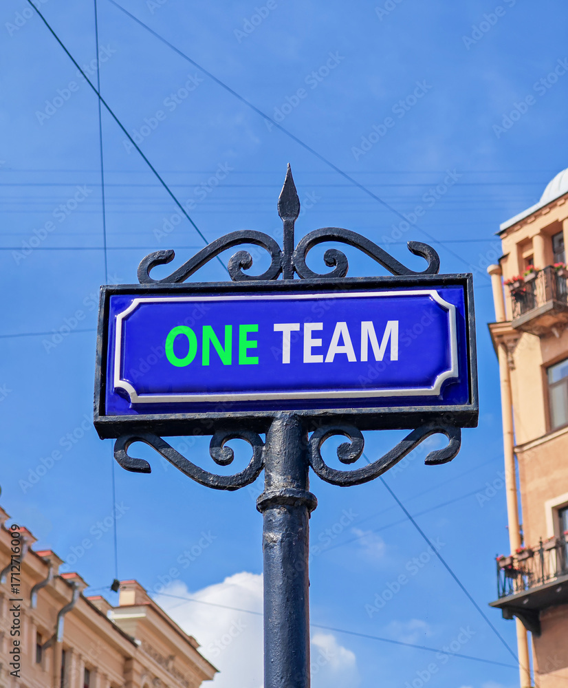 Obraz premium One team symbol. Concept word One team on beautiful blue road sign. Beautiful blue sky and buildings background. Business one team concept. Copy space.