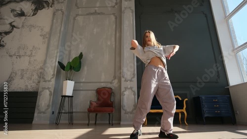 Stylish talented young woman dancing contemporary hip-hop in a spacious, sunny studio, performing an energetic and expressive choreography with modern street dance moves and passion
