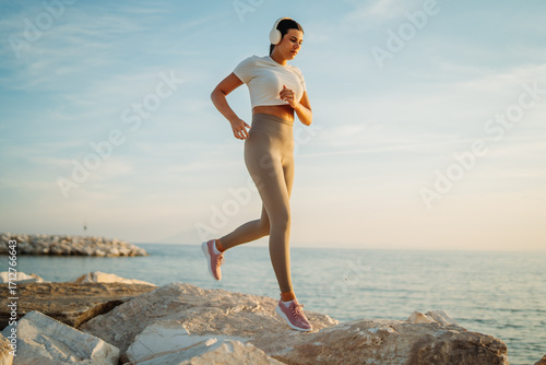 Young caucasian woman running on the stones by the beach at sunset 