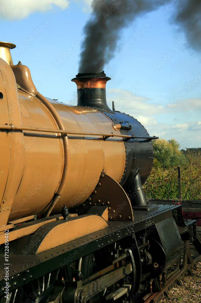 Naklejka premium Old vintage locomotive steam railway train engine with smoke blowing from its chimney funnel, travel transport stock photo image