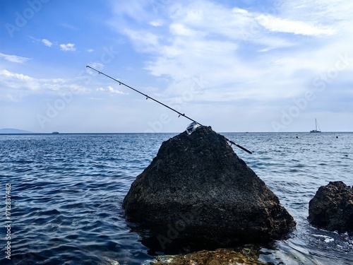 A fishing rod thrown into the sea and left on a rock. fishing rod propped up among rocks with the sea in the background