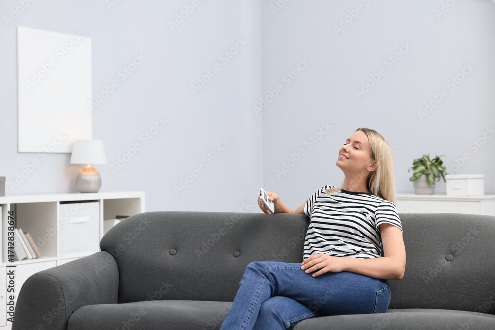 Obraz premium Woman with air conditioner remote control on sofa at home