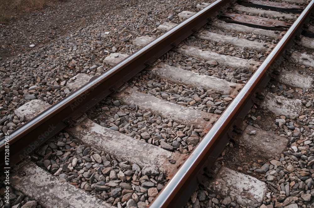 Naklejka premium Close-up of weathered railway tracks featuring stones and concrete ties