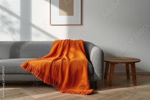Grey couch with an orange throw in a contemporary living room featuring a wooden table and wall art. Authentic photograph