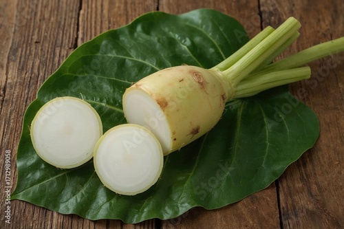 Fresh organic taro root placed on a wooden surface with a half slice on a leaf