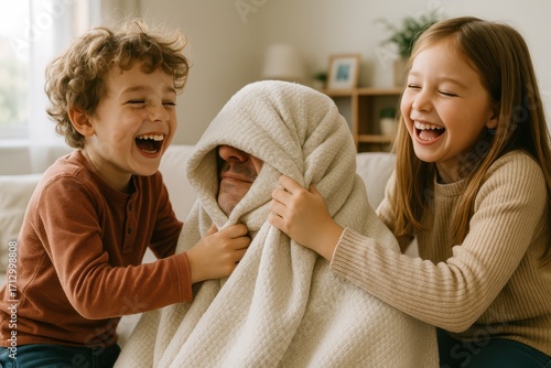 Two grandchildren laugh joyfully as they cover their grandfather with a blanket during a playful indoor game, creating a fun family moment.