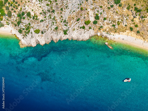 Hidden Croatian beach near Podgora protected by rocks with transparent lagoon textures and single boat anchored offshore