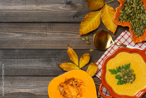 Pumpkin soup in bowl with autumn leaves and fresh pumpkin.