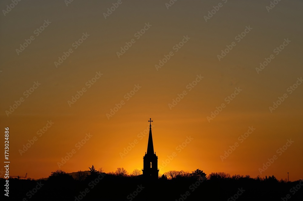 Obraz premium Sunset backdrop with a spire and cross silhouette on the horizon