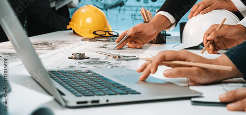A diverse engineering team collaborates on technical plans using a laptop and construction tools. The workspace reflects a modern and creative environment for innovative projects. SACTR