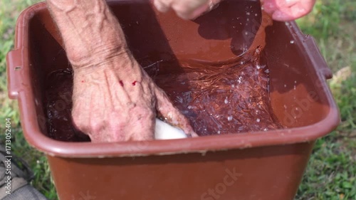 Elderly man with calloused and wounded hands washes away dirt with a bar of soap in a plastic basin on the street, his wife hands her husband a bar of soap,