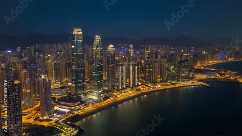 Night drone view of city lights near coast, cinematic wide aerial