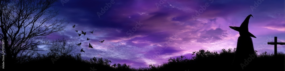 Fototapeta premium Halloween spooky night scene with a wizard hat silhouette, flying birds, bare tree, and graveyard cross against a dramatic purple sunset sky.