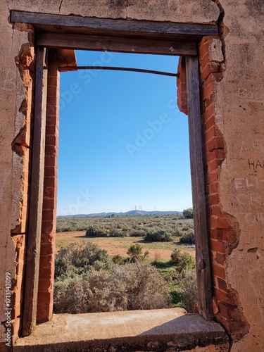 View through the window of ruins of a stone building overlooking the Australian outback. A blue sky over desert and saltbush plants. Taken near Silverton in New South Wales