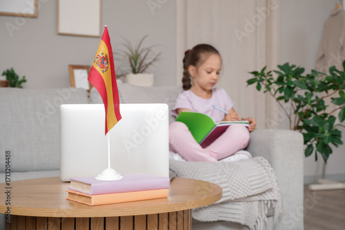 Little girl with laptop and copybooks attending online Spanish language lesso...
