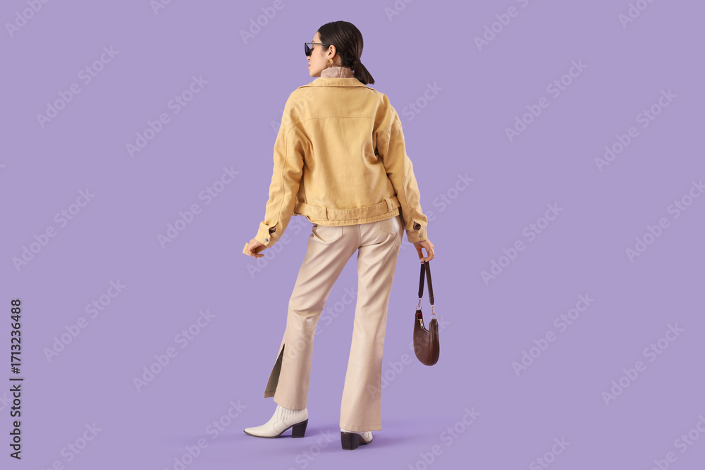 Fototapeta premium Young woman in stylish jacket on lilac background, back view