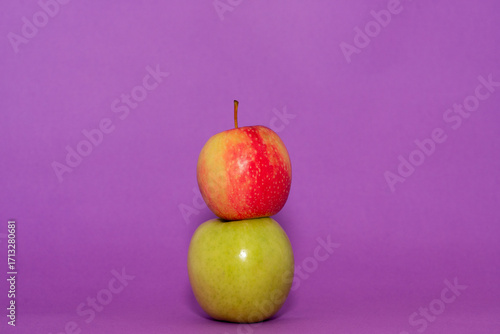 red and green apples stacked on a plain purple background