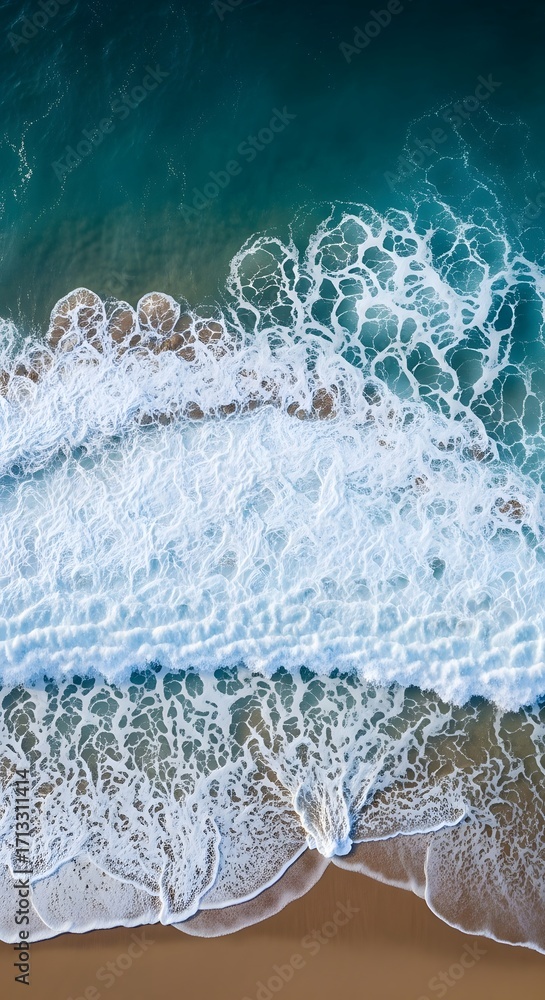 Naklejka premium High-angle view of foamy waves crashing on a sandy beach.