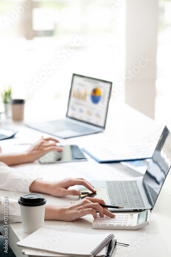 A professional is working at a modern office desk, typing on a laptop with documents and a coffee cup nearby. focused on business tasks, data analysis, and office productivity.