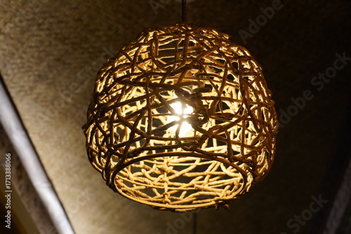 A beautifully crafted, handmade bamboo or rattan pendant lamp hangs from the ceiling, its warm, glowing light creating a cozy and inviting atmosphere. 