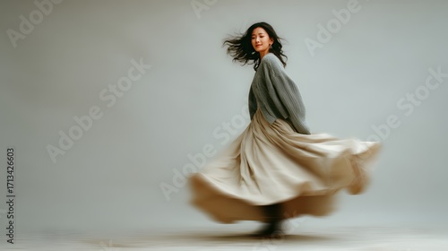 Asian woman in a flowing skirt twirling against a plain background. Motion blur captures the movement of the skirt, soft and elegant, autumn fashion 