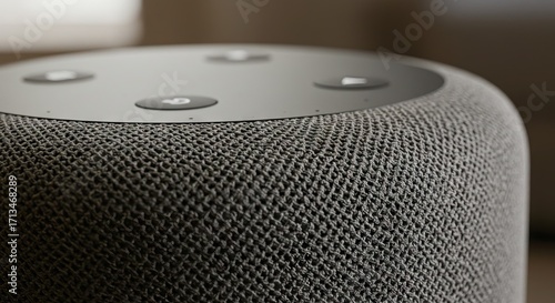 Closeup of a gray cylindrical smart speaker with a woven fabric exterior and black circular buttons on top