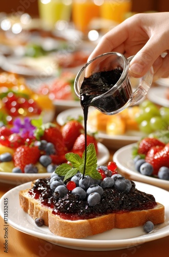 Hand pouring syrup over blueberry toast, amidst a colorful buffet with fruits and pastries. The scene creates a welcoming and appetizing breakfast spread