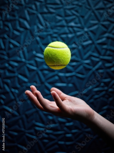 Tennis ball hovering above hand indoor studio sports photography dark background close-up gravity defying concept