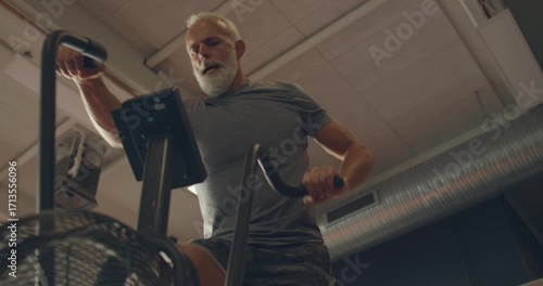 Low angle view of a fit mature man in
sportswear working out on a
stationary bike at the gym