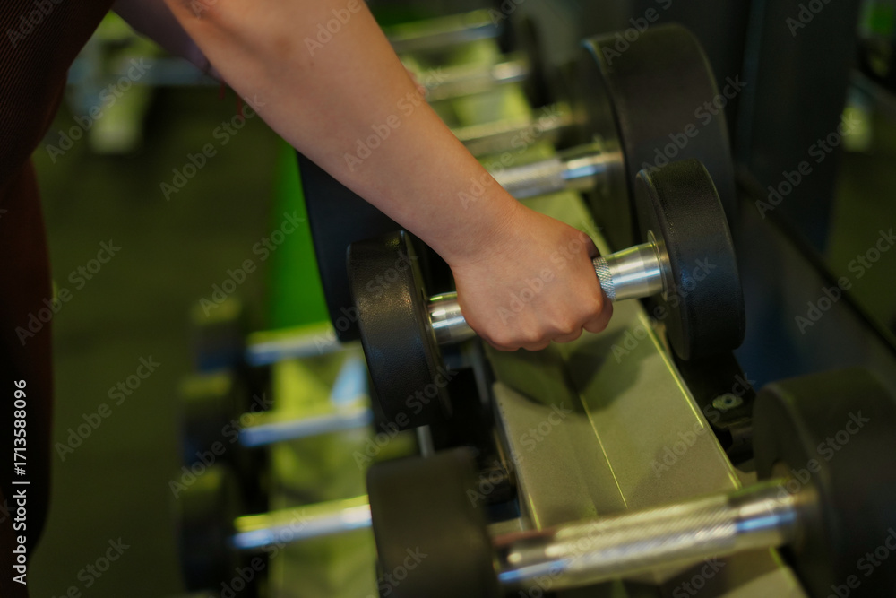 Fototapeta premium Person reaching for a dumbbell in gym for workout